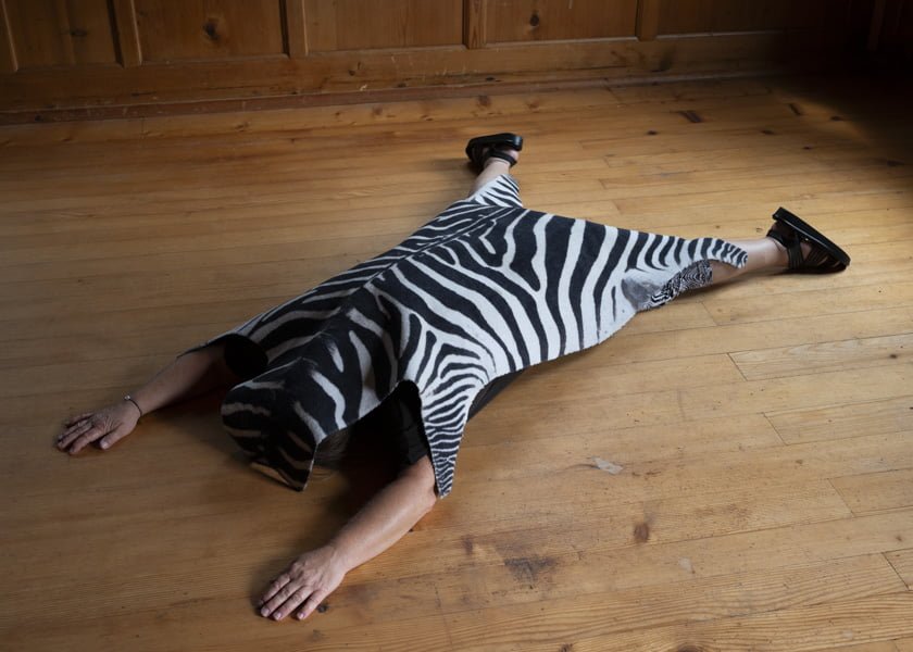 Eine Frau liegt auf einem alten Holzboden, unter einem Teppich mit Zebramuster.