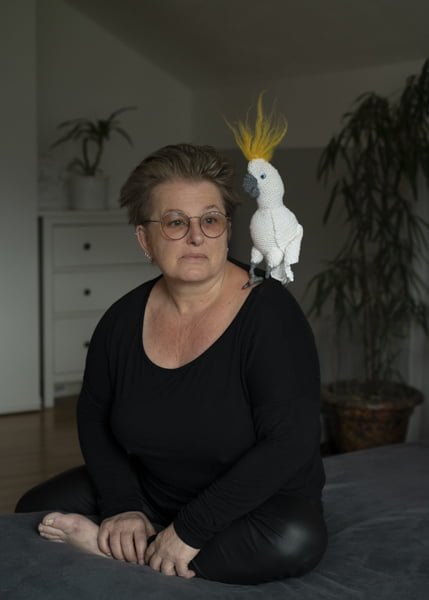 Eine Frau sitzt mit einem gehäkelten Kakadu auf dem Bett.